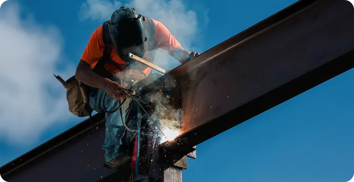 Integrated & Technical Services Construction worker welding a steel beam at height with sparks and protective gear.