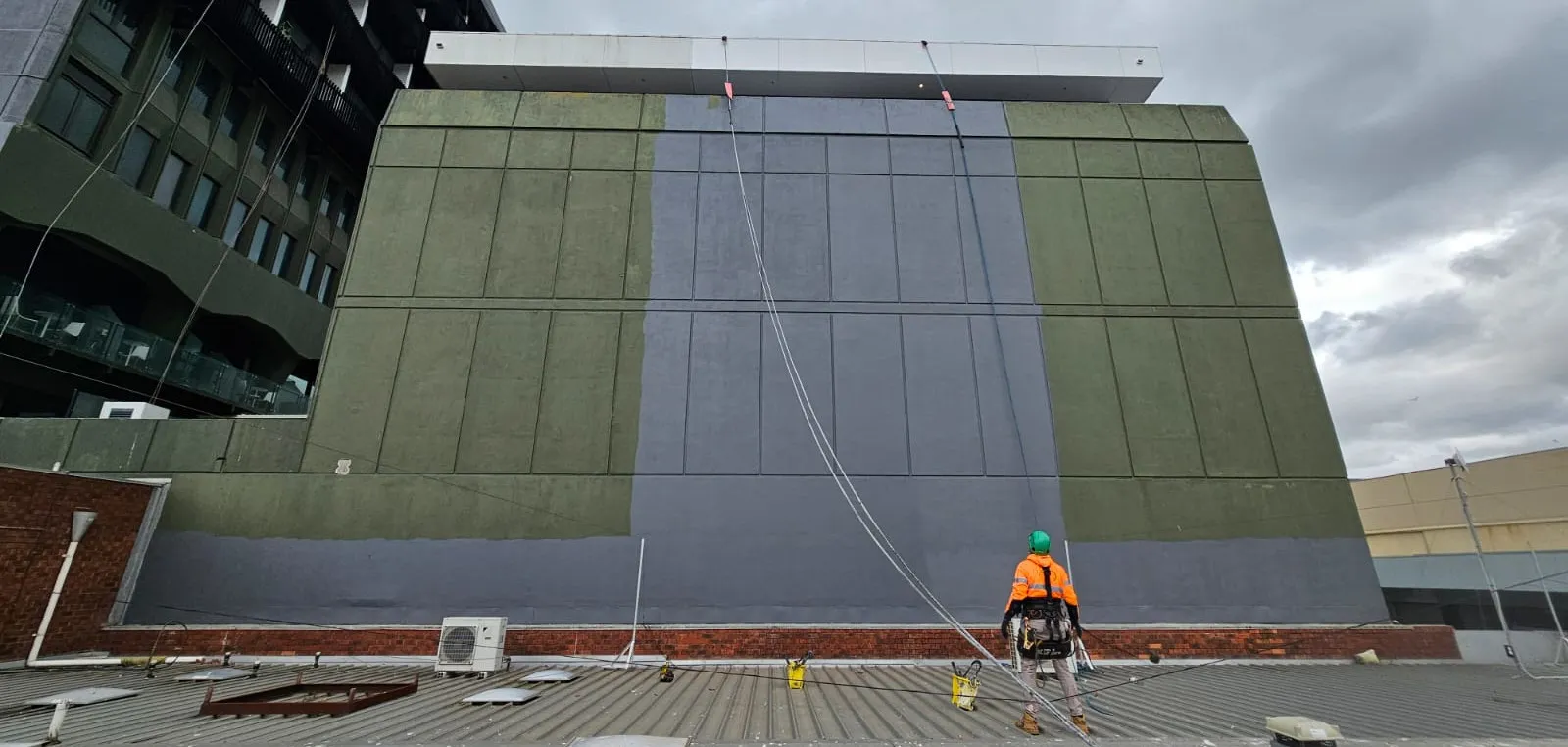 Rope-access technician preparing for facade painting or maintenance on a large commercial building wall.